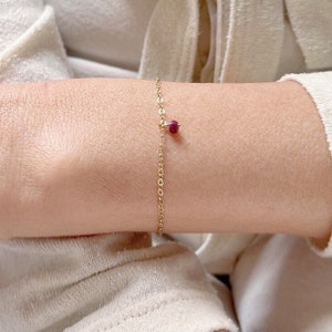 May include: A delicate gold chain bracelet with a small, round, red gemstone charm.