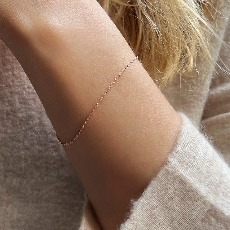 May include: A delicate gold chain bracelet on a person's wrist.