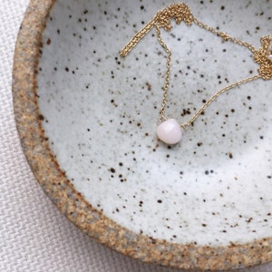 Pu&ograve; includere: Una delicata collana a catena dorata con un singolo ciondolo a forma di cuore in pietra preziosa rosa chiaro.