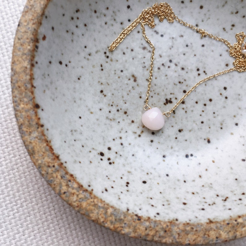 Pu&ograve; includere: Una delicata collana a catena dorata con un singolo ciondolo a forma di cuore in pietra preziosa rosa chiaro.