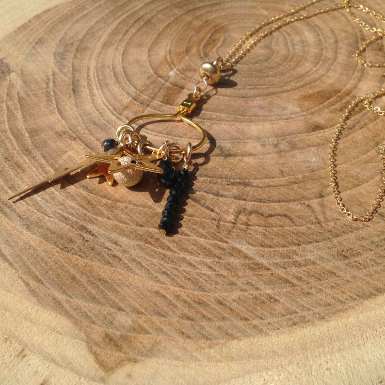 May include: A gold chain necklace with a charm circle and multiple charms, including stars, a lightning bolt, and black beads.