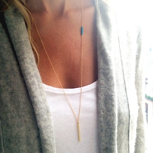 May include: A gold chain necklace with a long, thin gold bar pendant and a small row of turquoise beads.