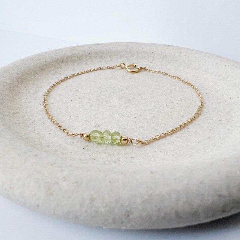 Op de afbeelding: Een delicate gouden kettingarmband met een rij lichtgroene peridoot edelstenen.