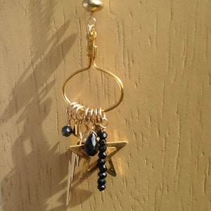 May include: Gold hoop earring with a dangling star charm and black beads. The star charm has a lightning bolt design.