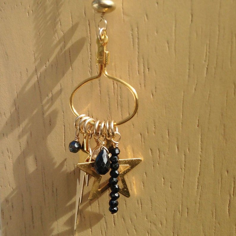May include: Gold hoop earring with a dangling star charm and black beads. The star charm has a lightning bolt design.