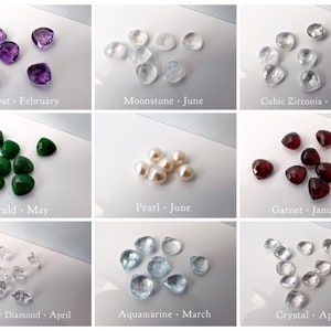 May include: Assortment of heart-shaped gemstones in various colors, including amethyst, moonstone, cubic zirconia, emerald, pearl, garnet, herkimer diamond, aquamarine, and crystal. Each gemstone is labeled with its name and corresponding birth month.