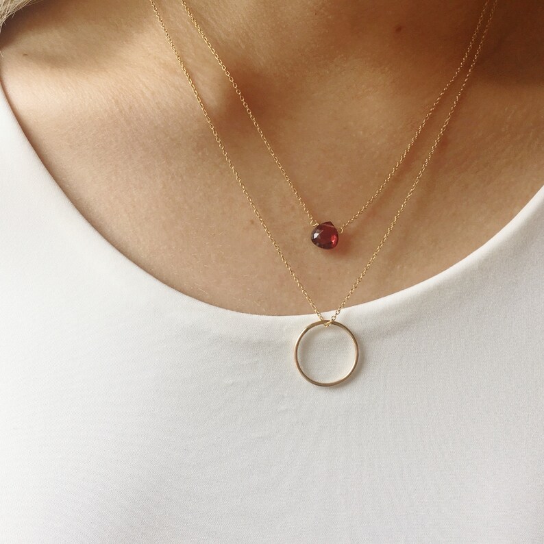 May include: A gold necklace with a small red gemstone pendant and a gold circle pendant.
