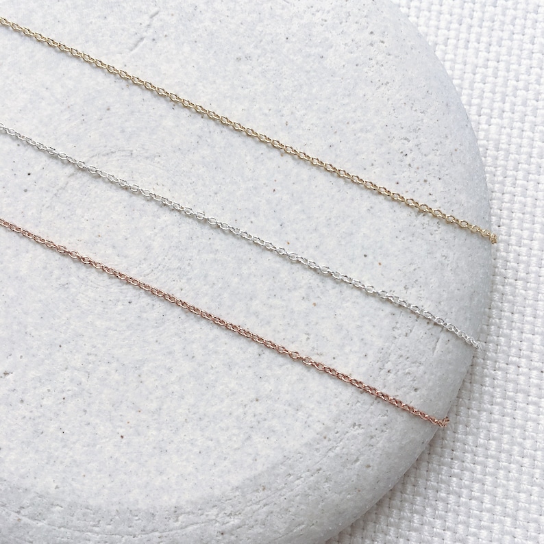 Pu&ograve; includere: Tre delicate collane a catena in oro, argento e oro rosa, mostrate su uno sfondo di pietra bianca.