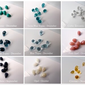 May include: Assortment of teardrop-shaped gemstones in various colours, including turquoise, blue topaz, cubic zirconia, pink opal, sapphire, opal, and citrine. Each gemstone is labelled with its name and corresponding birth month.