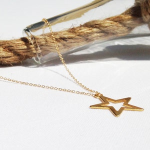 May include: A gold chain necklace with a star-shaped pendant. The star is open in the center, creating a double-layered effect.