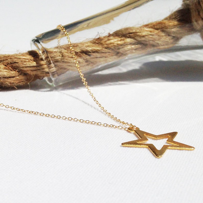 May include: A gold chain necklace with a star-shaped pendant. The star is open in the center, creating a double-layered effect.