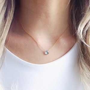 May include: A delicate gold chain necklace with a single, light blue gemstone pendant.