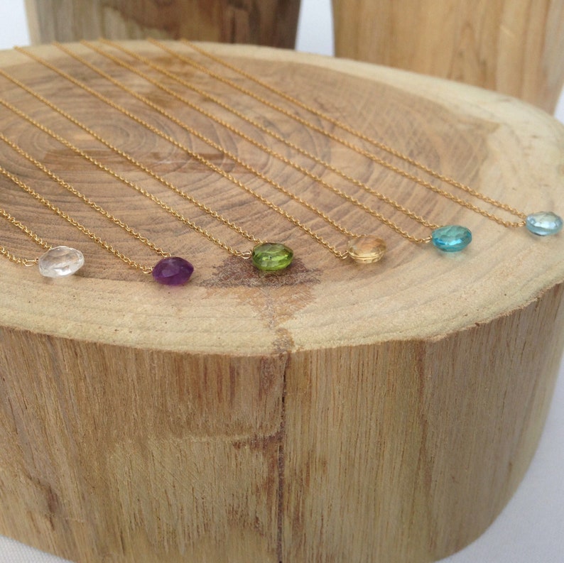 Puede incluir: Un conjunto de nueve collares de oro con colgantes de piedras preciosas de diferentes colores. Los colgantes son transparentes, morados, verdes, amarillos, azules y azul claro.