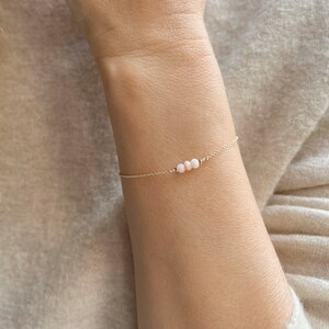 Peut inclure: Un bracelet délicat en chaîne dorée avec trois petites perles d'opale rose.