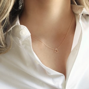 A dainty open heart charm is sitting on a minimalist gold filled dainty chain.