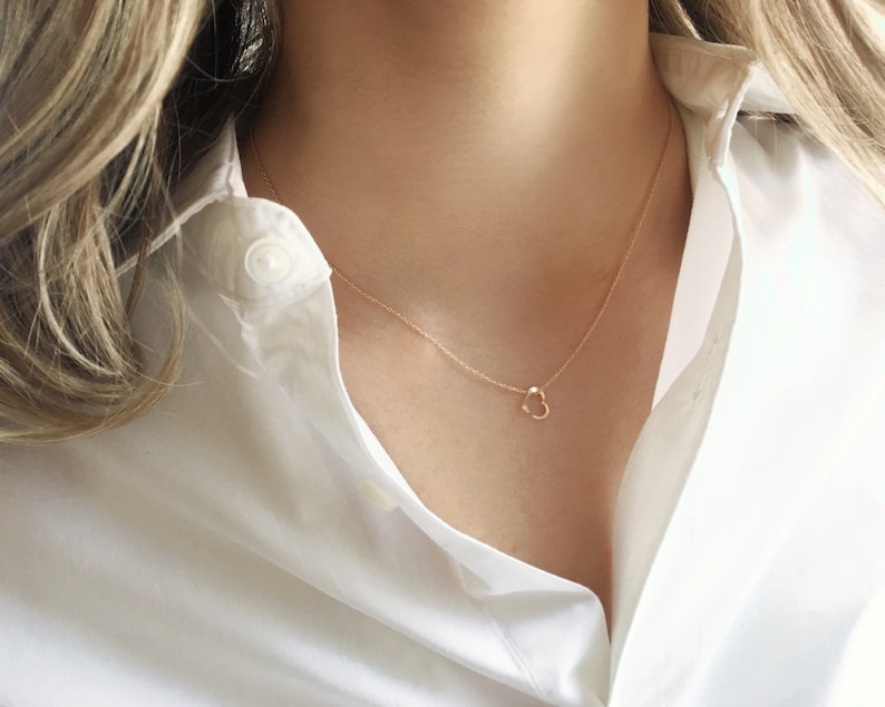 A dainty open heart charm is sitting on a minimalist gold filled dainty chain.