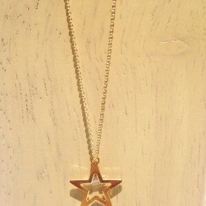 May include: A gold chain necklace with a gold star pendant. The star is open in the middle, creating a hollow center.