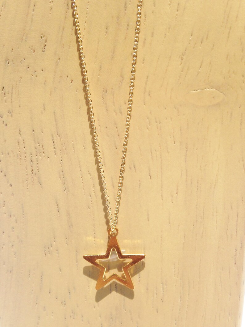 May include: A gold chain necklace with a gold star pendant. The star is open in the middle, creating a hollow center.