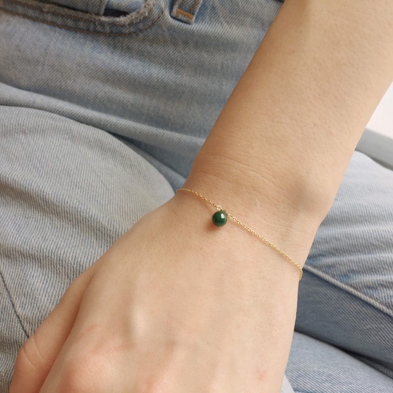May include: A delicate gold chain bracelet with a single, round green gemstone pendant.