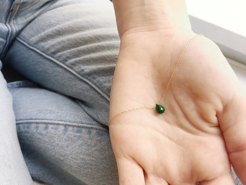 May include: A delicate gold chain necklace with a small, teardrop-shaped green gemstone pendant.