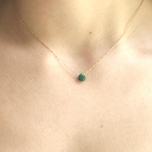 Puede incluir: Un delicado collar de cadena de oro con un pequeño colgante de piedra preciosa verde oscuro.