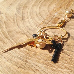 May include: Gold charm necklace with a variety of charms, including stars, a lightning bolt, and black beads.