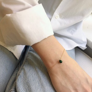 May include: A delicate gold chain bracelet with a single teardrop-shaped green gemstone pendant.