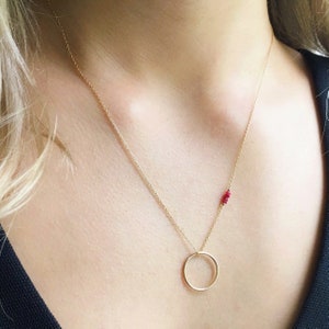 May include: A gold chain necklace with a small circle pendant and a cluster of red gemstones.