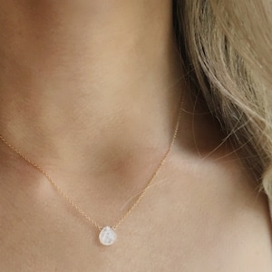 May include: A delicate gold chain necklace with a single teardrop-shaped clear gemstone pendant.