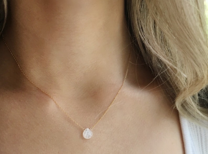 May include: A delicate gold chain necklace with a single teardrop-shaped clear gemstone pendant.