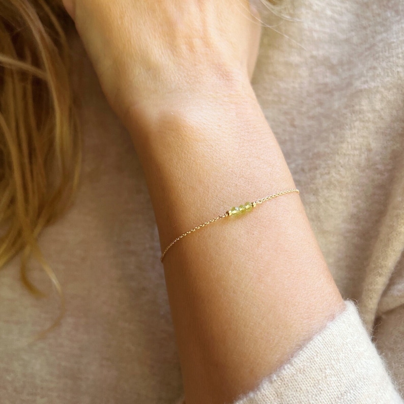Op de afbeelding: Een delicate gouden kettingarmband met een kleine cluster van lichtgroene edelstenen.