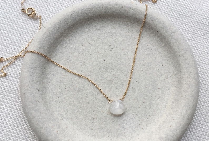 May include: A delicate gold chain necklace with a single, round, white gemstone pendant.