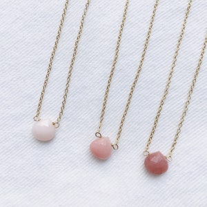 Pu&ograve; includere: Tre collane d'oro con pietre a forma di cuore rosa. Le collane sono su uno sfondo bianco.