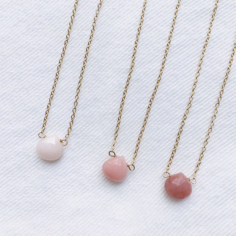 Pu&ograve; includere: Tre collane d'oro con pietre a forma di cuore rosa. Le collane sono su uno sfondo bianco.