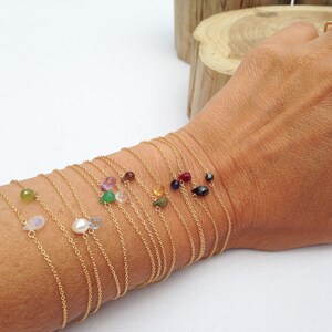 May include: A set of delicate gold chain bracelets with small gemstone accents. Each bracelet features a different gemstone, including amethyst, emerald, and sapphire.