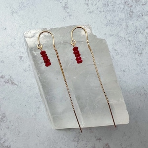 May include: A pair of gold dangle earrings with a small cluster of red ruby beads at the top of each earring.