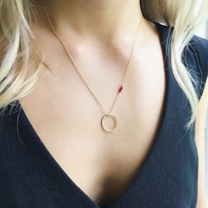 Puede incluir: Un collar de oro con un colgante circular y un pequeño racimo de cuentas rojas.