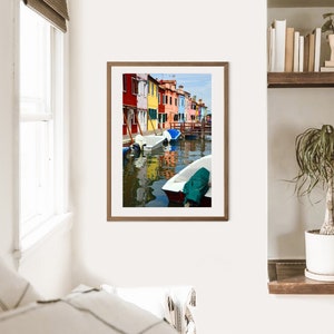 Könnte beinhalten: Ein gerahmtes Foto von bunten Häusern, die einen Kanal säumen, mit Booten, die im Wasser liegen. Die Häuser sind in den Farben Rosa, Gelb, Blau, Grün und Rot gestrichen. Das Wasser ist klarblau und der Himmel strahlend blau.