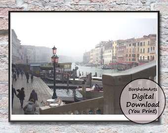 May include: A foggy view of a canal in Venice, Italy. The canal is lined with colorful buildings and boats. A lamppost stands on the edge of the canal, and people are walking along the sidewalk.