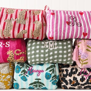 May include: A collection of quilted fabric pouches in various patterns including leopard print, stripes, gingham, and floral designs. Each pouch features personalized embroidery with names or initials such as MIA, R, R.S, AML, Mireya, and MA.