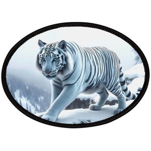 May include: Oval patch featuring a white tiger with black stripes walking on a snowy mountain. The tiger has blue eyes and a pink nose. The background shows a snowy landscape and a foggy sky. The patch is framed by a black border.