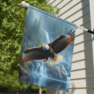 May include: A decorative outdoor flag featuring a majestic bald eagle in flight. The eagle has brown and white feathers, with a yellow beak and eyes. The background depicts a waterfall and forest scene, with a blue sky.
