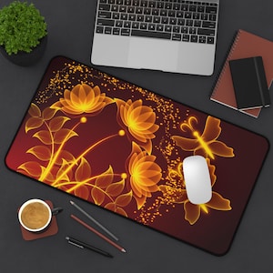 Könnte beinhalten: Eine rechteckige Schreibtischunterlage mit dunkelrotem Hintergrund, einem leuchtend orange-gelben Blumenmuster und Schmetterlingssilhouetten. Die Unterlage ist mit Lichtpartikeln verziert und liegt auf einem Schreibtisch mit Laptop und Notizbüchern.