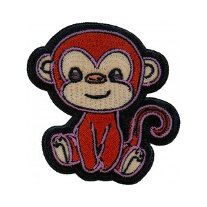 May include: Embroidered patch featuring a cartoon monkey in a seated position. The monkey is primarily red with a light tan face, pink accents, and a black outline. The patch is designed with a smiling expression.