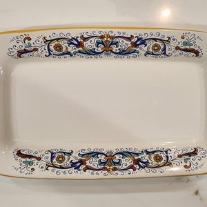 May include: Rectangular white ceramic serving platter with a decorative floral and scroll design in blue, yellow, and brown. The rim is outlined in gold, and the sides have vertical brown dashes.