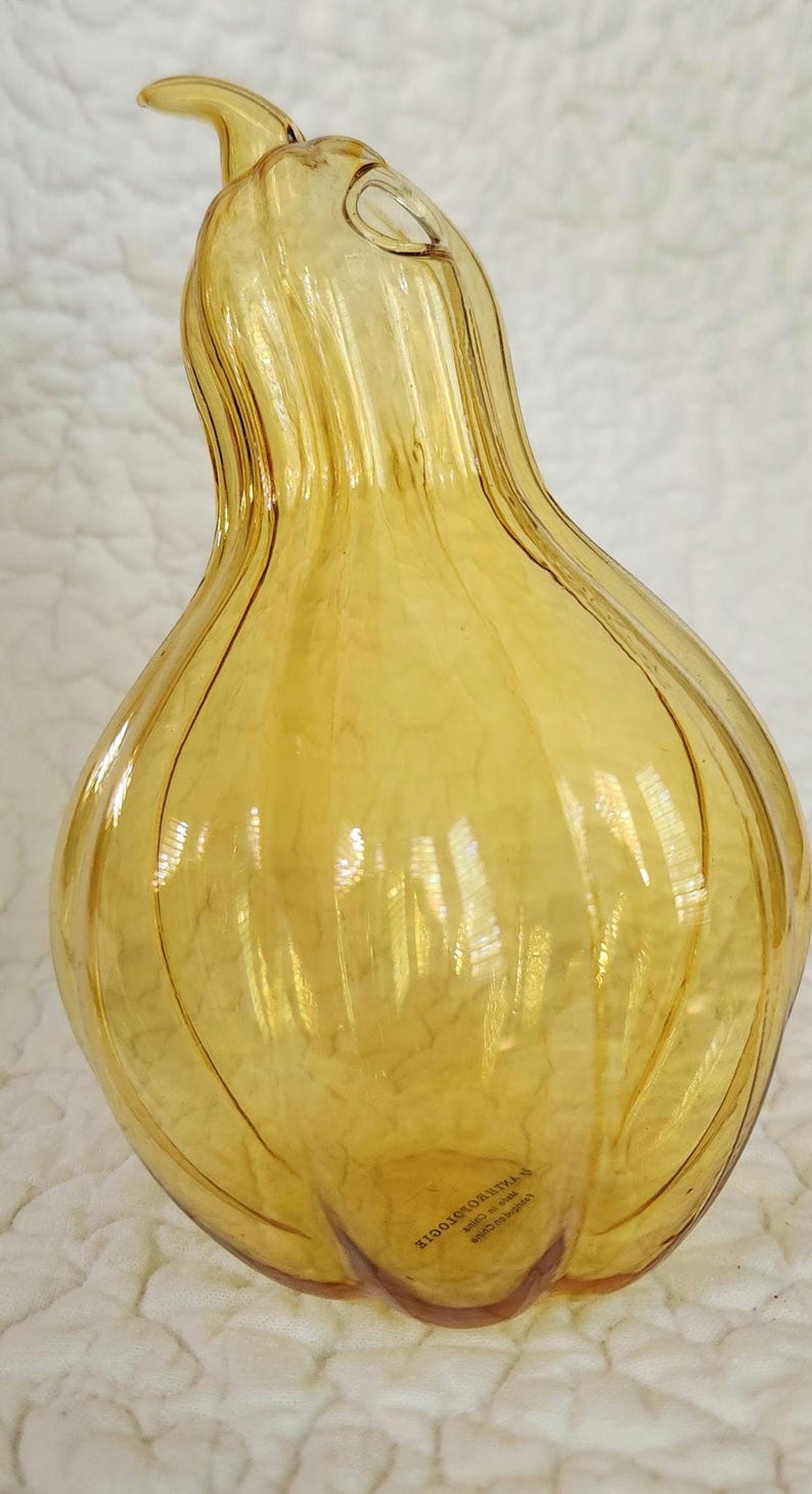 May include: A decorative, amber-colored glass vase with a bulbous body and a slender, curved neck. The vase has vertical ridges and a small opening at the top. The vase is approximately 12 inches tall.