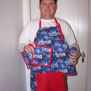 May include: A blue and red apron with a Patriots logo and two matching pot holders. The apron has a large pocket on the front.