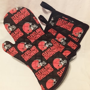 May include: A set of two black oven mitts with a quilted design. The mitts feature a repeated pattern of the Cleveland Browns logo, which includes a red football helmet and the words "Cleveland Browns".