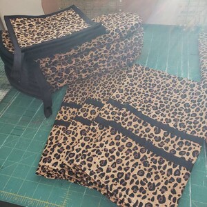 May include: A stack of leopard print fabric squares with black trim, and a stack of leopard print fabric rectangles with black stripes.