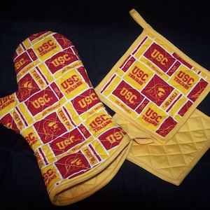 May include: A set of two yellow and red oven mitts with the USC Trojans logo and the words "Fight On!" repeated throughout the design.